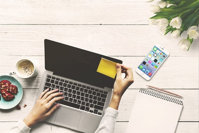 A woman holding a post-it in one hand and working on a laptop